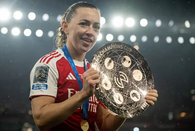 Katie McCabe holds up the trophy (a golden disk)
