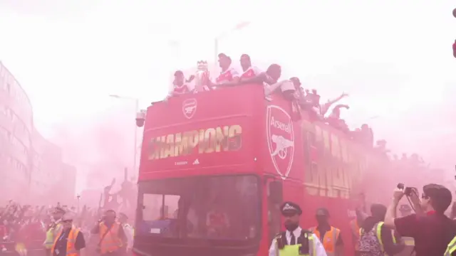 Red smoke fills the air as the bus with the Premier League trophy passes