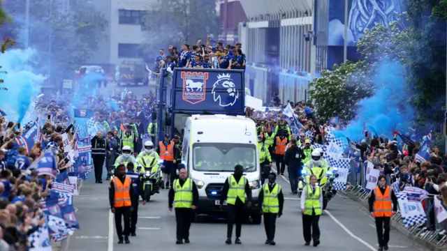 Fans line the streets behind metal barriers as the Ipswich Town parade bus comes through the streets.