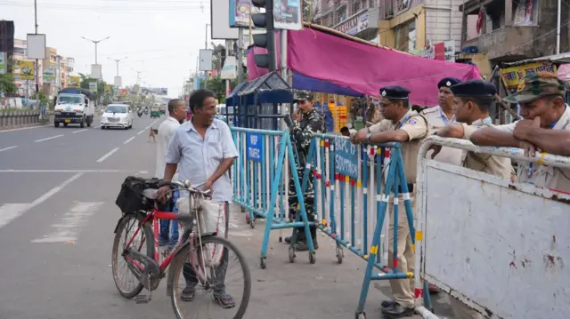 A man walks with his cycle as police personnel stand next to barricades