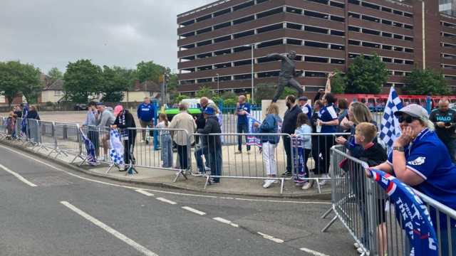 Crowds of people starting to build at metal fencing at Portman Road Stadium.