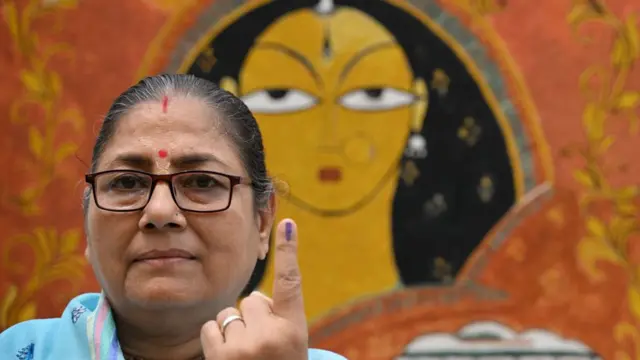 A woman wearing a saree and glasses shows her inked finger after casting vote