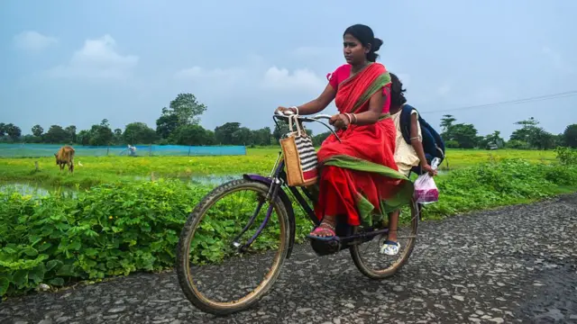 A lady rides a bicycle in cloudy weather on the outskirts of Kolkata, India, on June 29, 2025