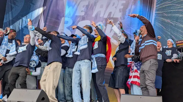 Players and manager singing with their arms in the air