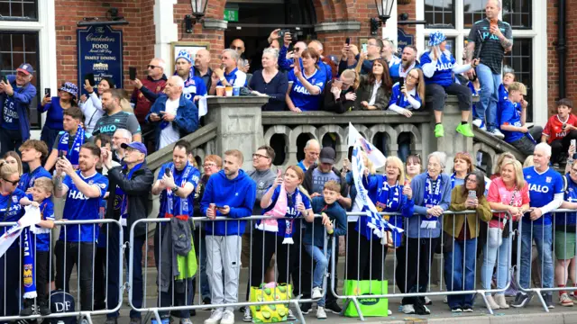 Crowds of fans inside a metal barrier outside a pub all trying to get a glimpse of the Ipswich Town parade bus