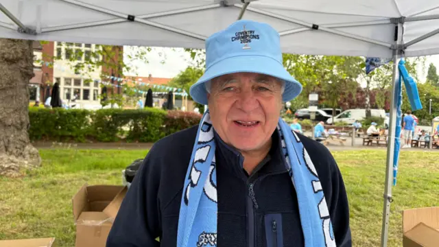 A man in a sky blue bucket hat with a scarf around his neck