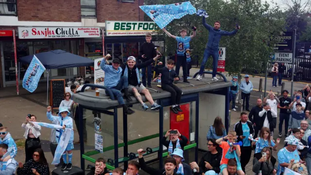 Coventry City fans on top of a bus stop during the parade as they celebrate promotion to Premier League