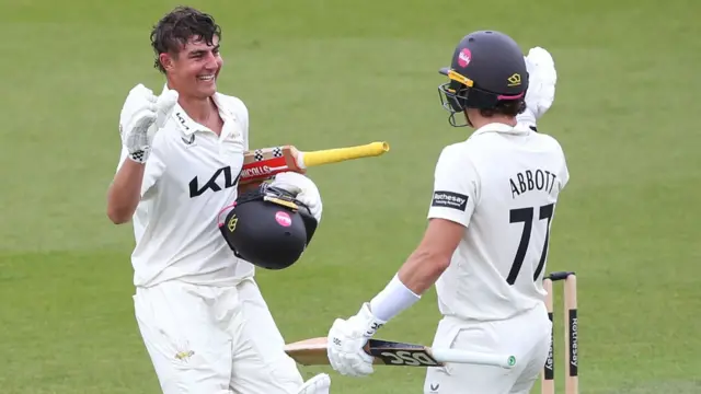 Surrey's Adam Thomas, without helmet in left hand, celebrates a century with Sean Abbott