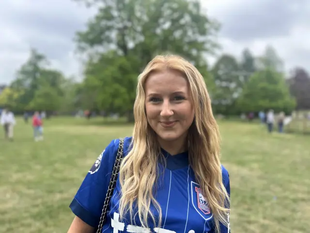 A woman with long blonde hair wearing a blue Ipswich Town football club shirt