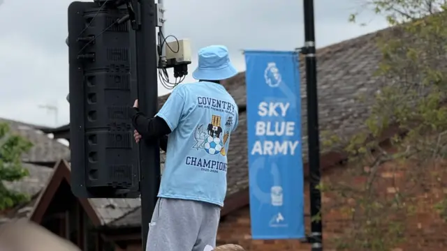 A person in a Sky Blue shirt and bucket hat, hands off a traffic light