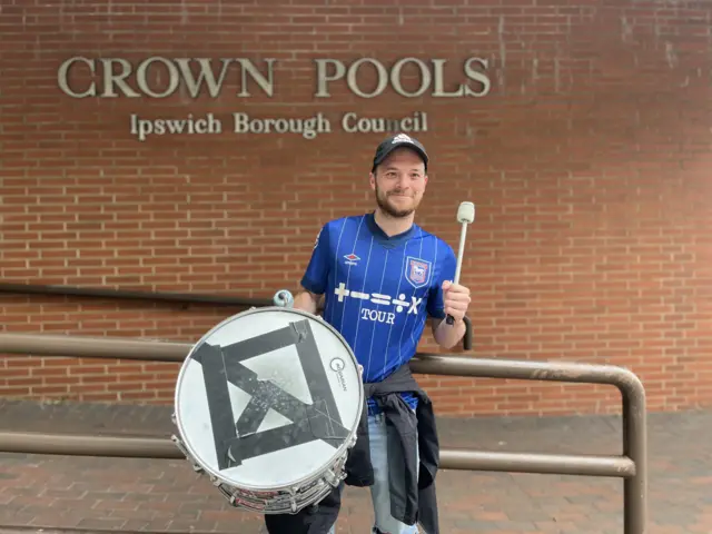 Nathan Parris with a drum standing outside Crown Pools in Ipswich. He is wearing an Ipswich Town football shirt.