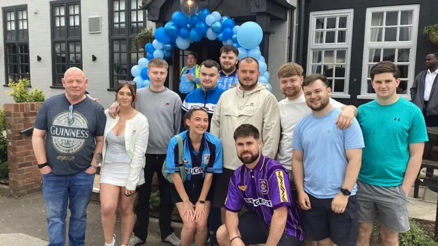 A group of people outside a pub, balloons around the entrance