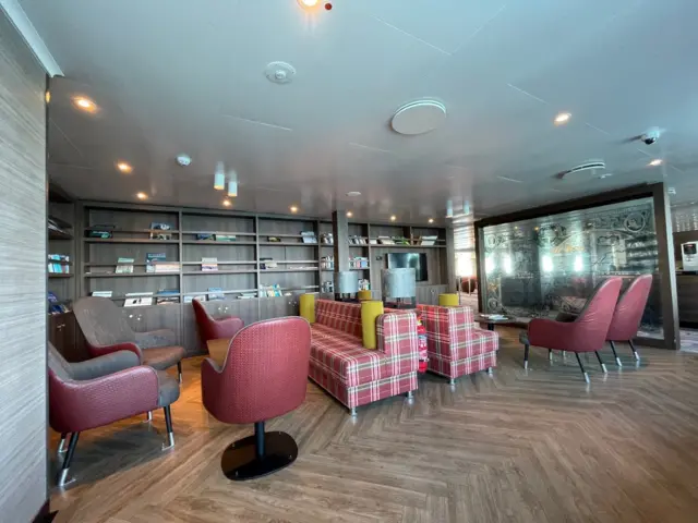 Interior of ship showing lounge area with lots of chairs and two sofas