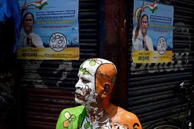 A TMC supporter with the party election symbol painted on his body sits next to posters of West Bengal Chief Minister Mamata Banerjee