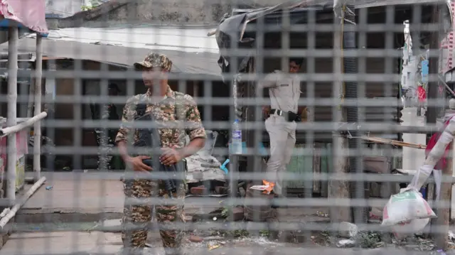 A security personnel stands with a gun in his hand behind a wired mesh