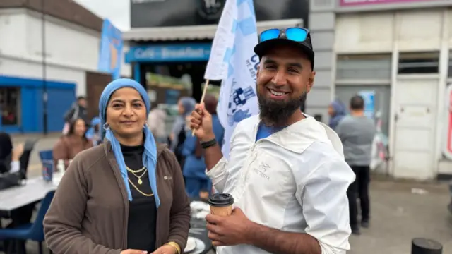 A woman and a man outside a cafe, the man holding a flag