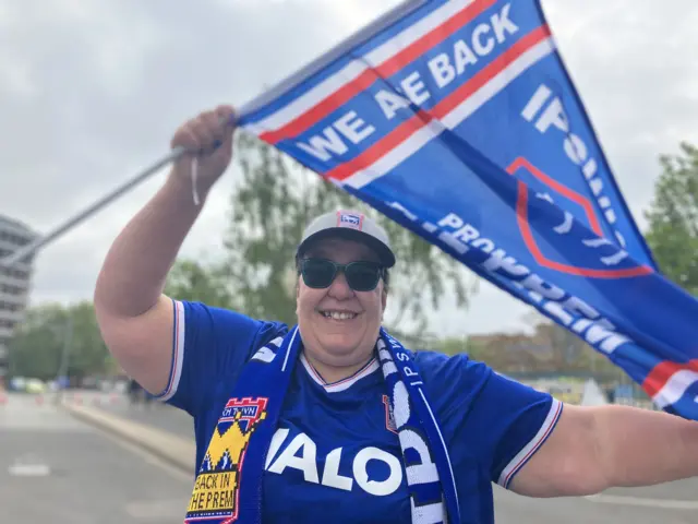 Nancy Hall De Vuyst in an Ipswich Town football shirt waving a flag in the air.