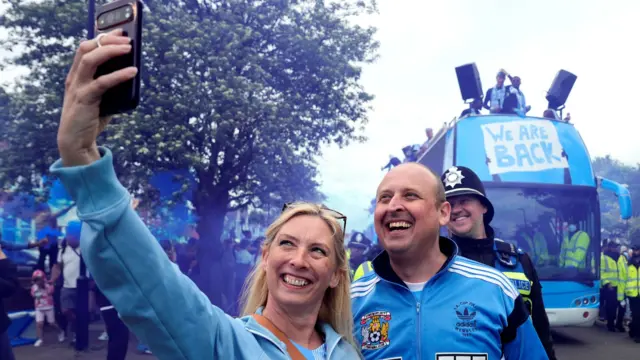Coventry City fans take photographs in front of the parade bus during a victory parade in Coventr