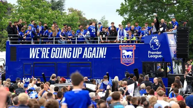 Crowds of people gather to see the Ipswich Town bus pass through the town.