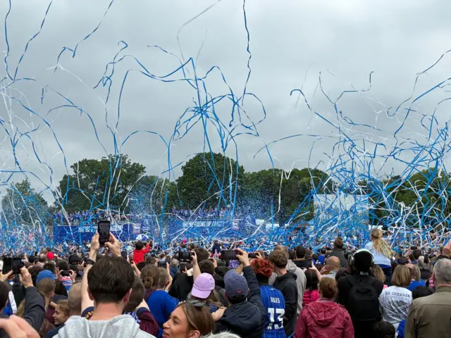 Blue and white streamers let off at Christchurch Park over the heads of crowds