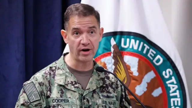 A man in green military fatigues standing in front of the Central Command logo