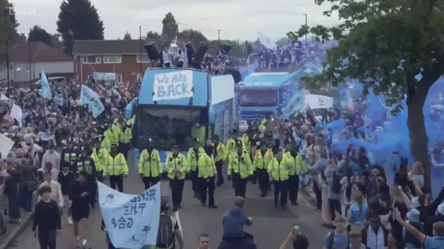 Police in front of two sky blue buses, surrounded by fans
