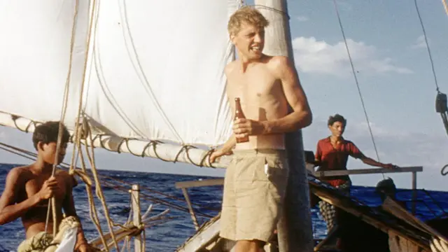 A young David Attenborough pictured holding a bottle on a small fishing boat