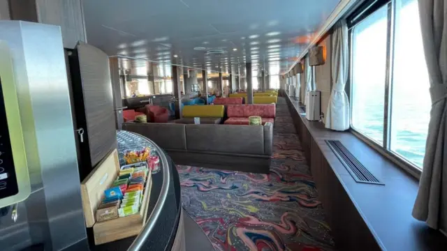 Rows of sofas near a snack bar and widows on board the MV Hondius.