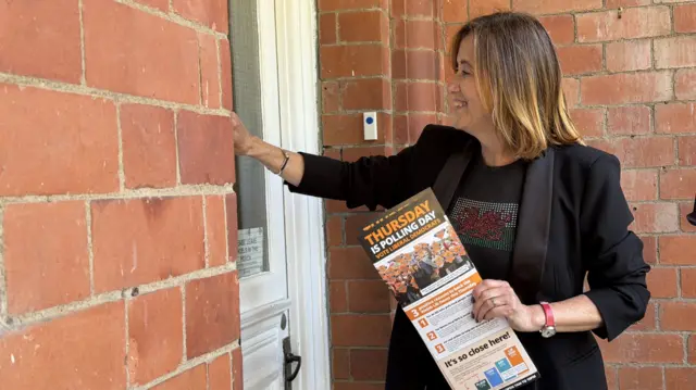 Jane Dodds knocks a door holding Lib Dem pamphlets