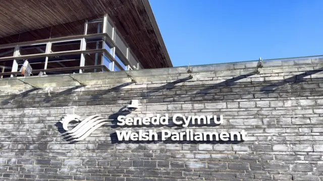 Picture of the Senedd and the sign "Senedd Cymru - Welsh Parliament" on the bricks of the building in Cardiff Bay