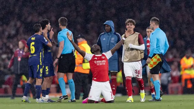 Bukayo Saka on his knees, looking towards the sky with arms aloft, celebrating at the final whistle