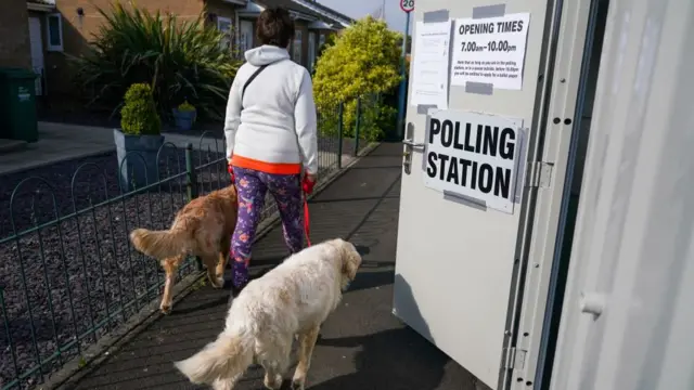 A woman walks past a polling station, with two Labrador retriever dogs on leads
