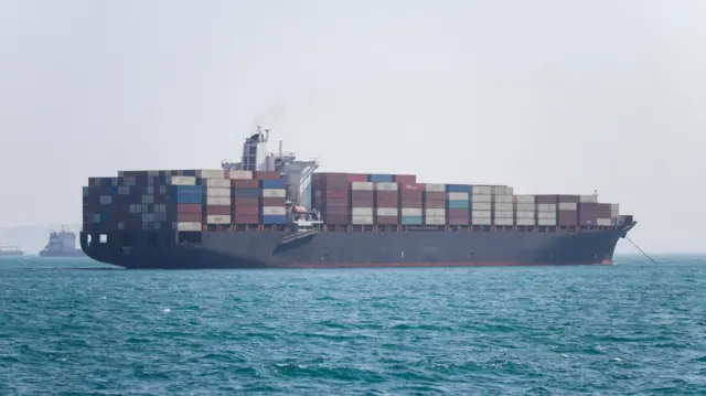A large cargo vessel loaded with containers is shown in the Strait of Hormuz.
