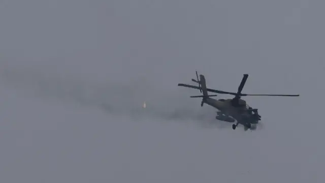 An Israeli helicopter is shown in the air, firing its cannon - smoke trails behind.