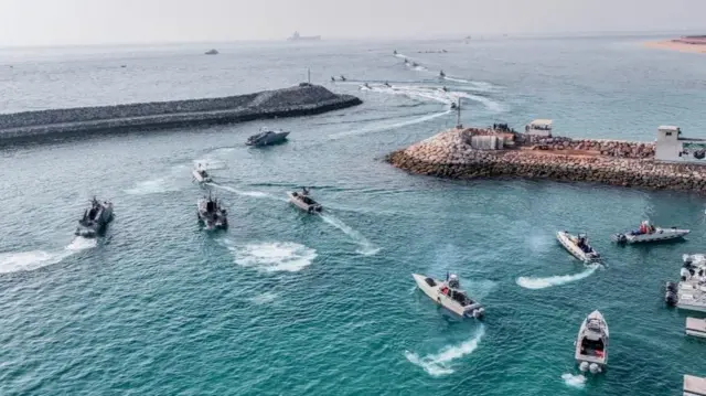 Around a dozen small speedboats are shown departing from an Iranian port.