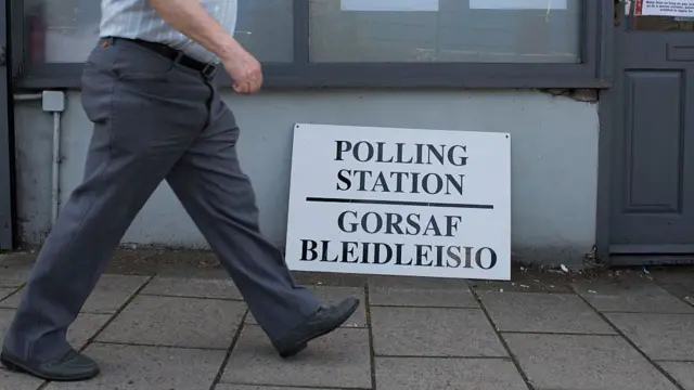 A man walks past a sign that reads "polling station" in English and "gorsaf bleidleisio" in Welsh