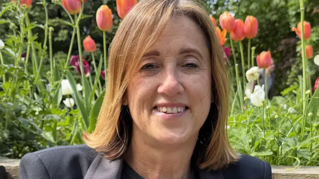 Jane Dodds sat in front of a flower bed wearing a black jacte