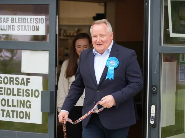 Darren Millar wearing a white shirt, navy jacket and a blue badge.
