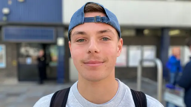 A headshot of Caleb Anderson who wears a cap and smiles at the camera