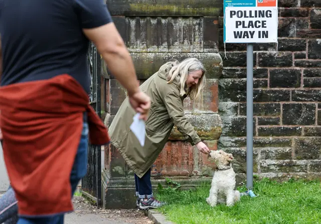 A woman leans over to give a dog a treat