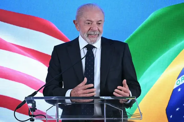 President Lula of Brazil speaks into microphones in front of a screen showing US and Brazilian flags