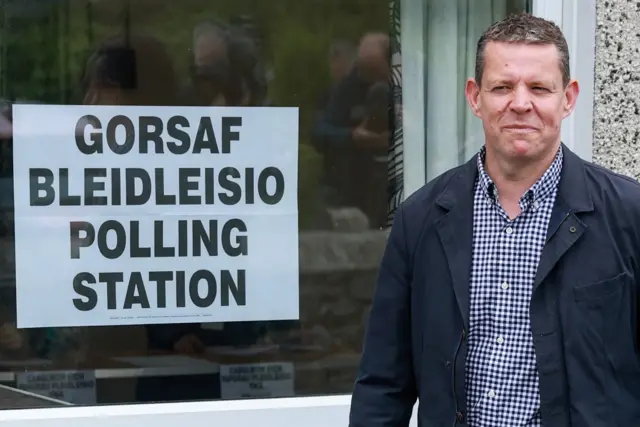Rhun ap Iorwerth standing beside a Polling station sign.