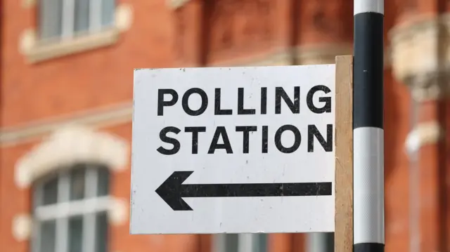 A polling station direction sign is attached to a pedestrian crossing