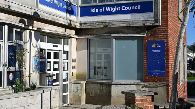 An external picture of the Isle of Wight Council building. It is a brick and stone building with a blue and white Isle of Wight Council sign.