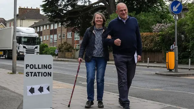 Britain's Liberal Democrats party leader Ed Davey (R) arrives with his wife Emily Davey to cast their votes at a polling station at Surbiton Hill Methodist Church, southwest London on May 7, 2026.