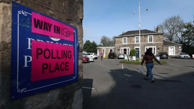 A voter arrives at a polling station in Edinburgh, Scotland, where there is signage pointing to the entrance