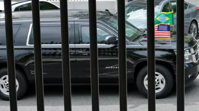 black SUV, with American and Brazilian flags on it, driving on a road as it leaves White House