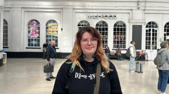 A girl in a black hoodie. She has glasses and died hair.