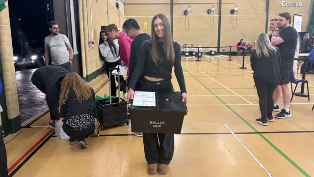 A young girl holding a ballot box in a leisure centre.