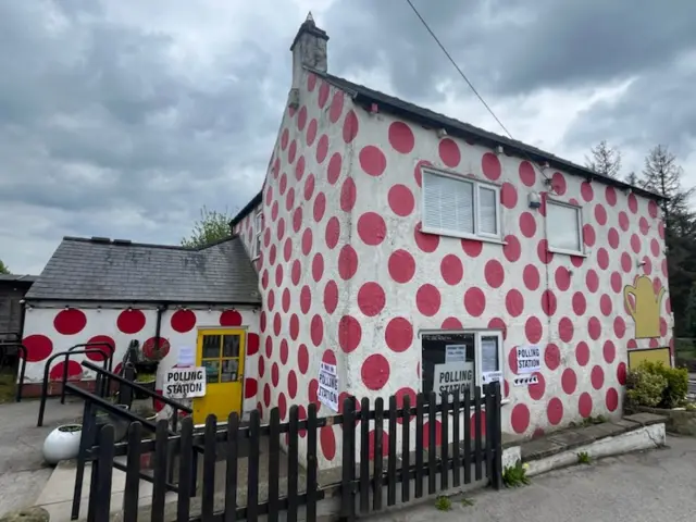 A red and white spotted two storey building with a sign reading Polling Station outside